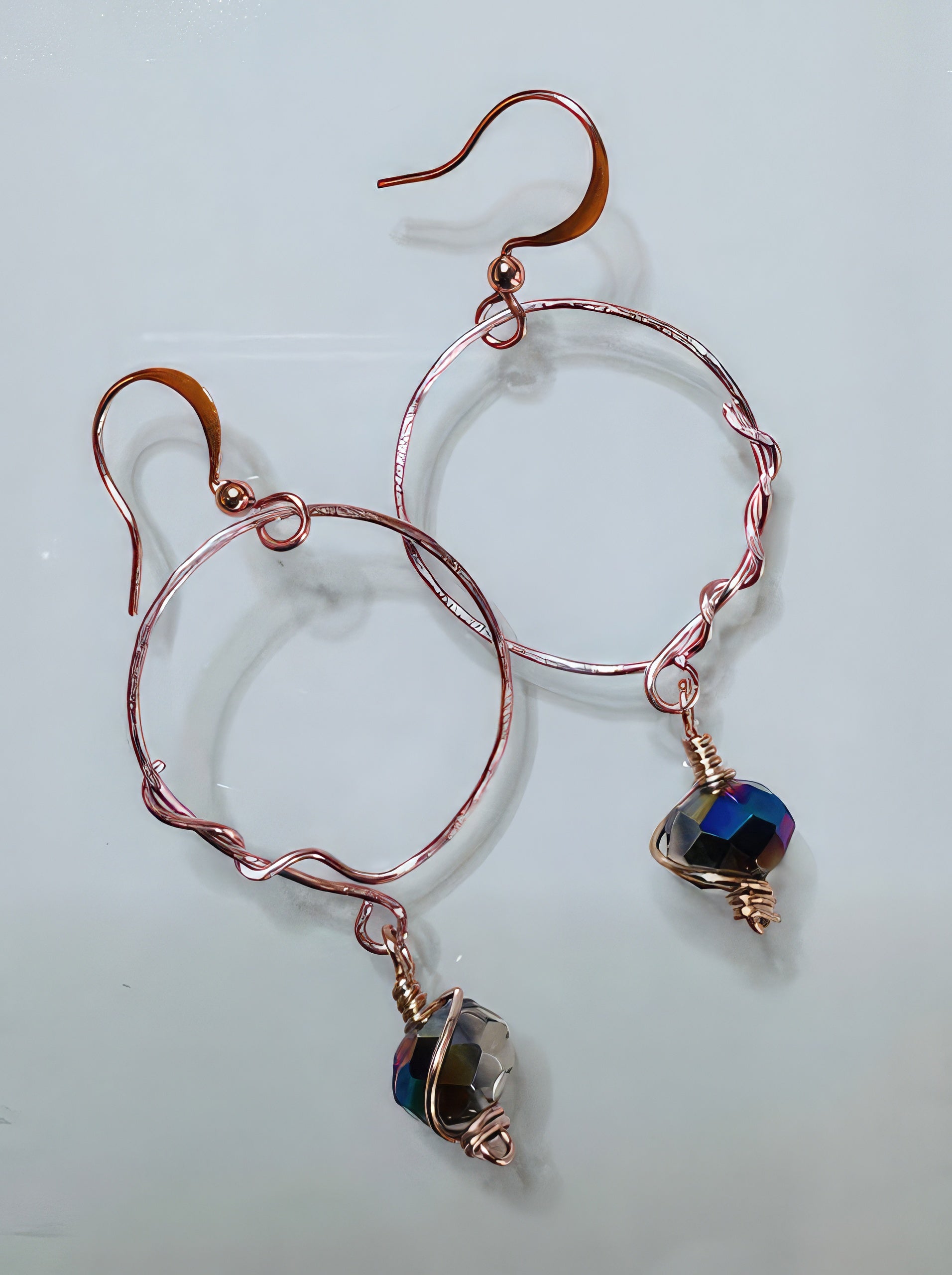 A pair of handcrafted earrings featuring wrapped copper wire and Czech glass beads in shades of purple, green, and clear, with a copper hoop design.