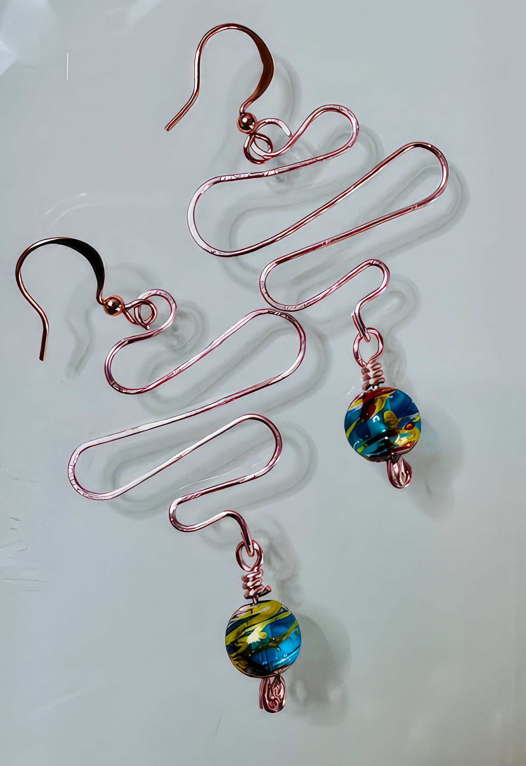 A pair of earrings with hand formed copper wire and a teal blue with hints of gold painted glass bead, suspended from copper core ear wires with a non-tarnish coating.