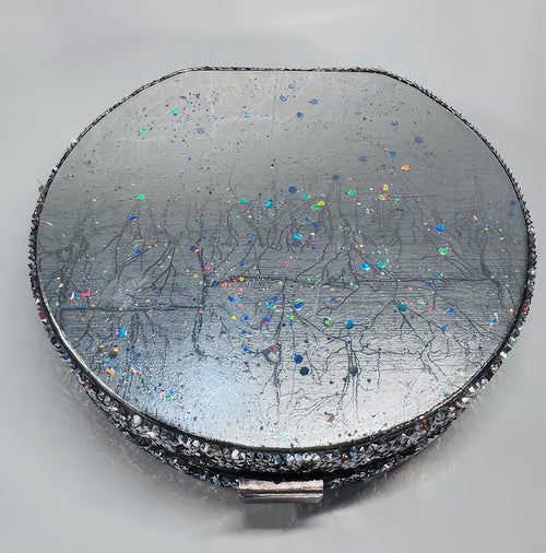 A round silver cross-body purse with multicolored faux stone embellishments and a metallic finish.