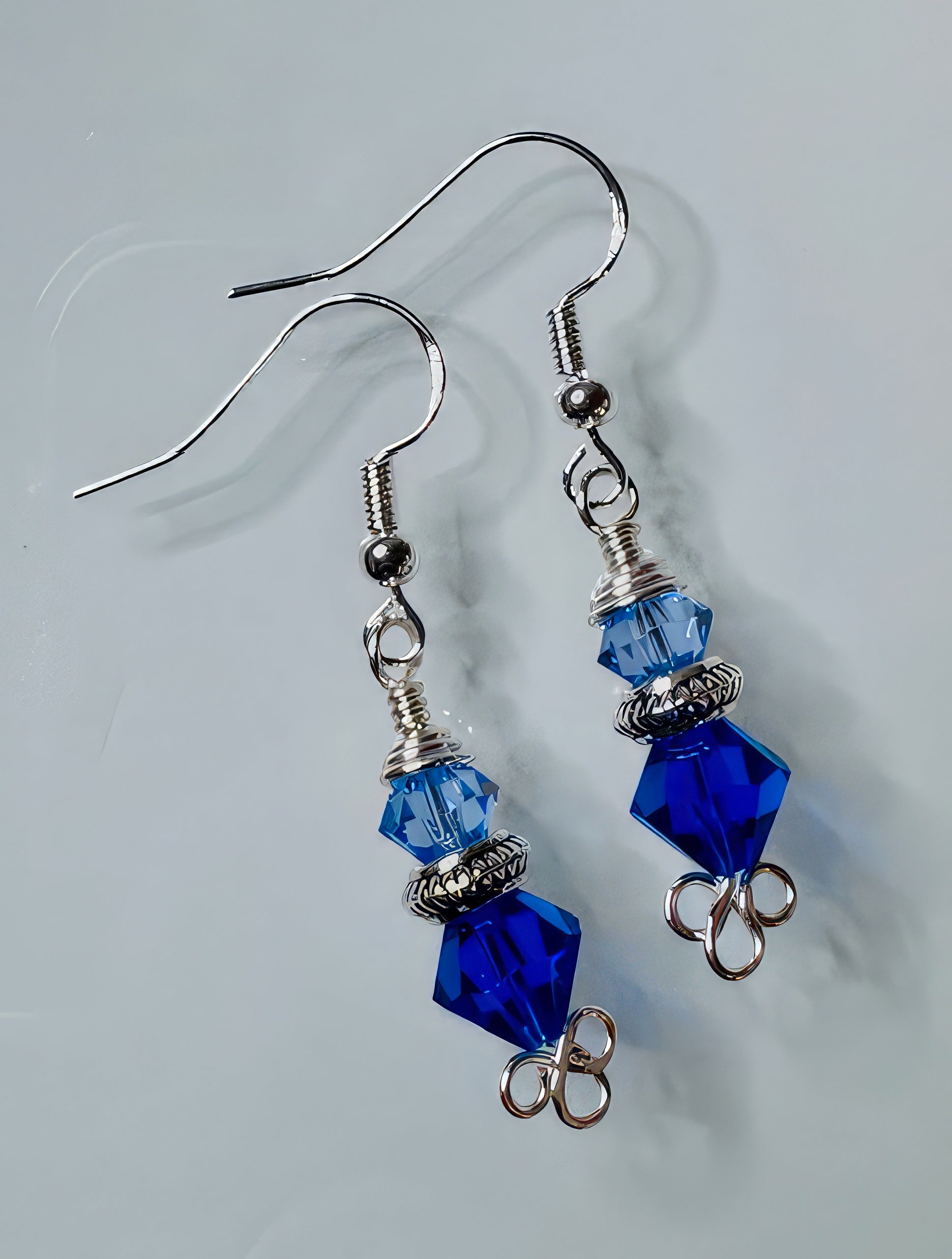 A pair of earrings featuring pale blue and medium blue Swarovski crystals, with sterling silver earwire and antiqued silver tone flat beads.