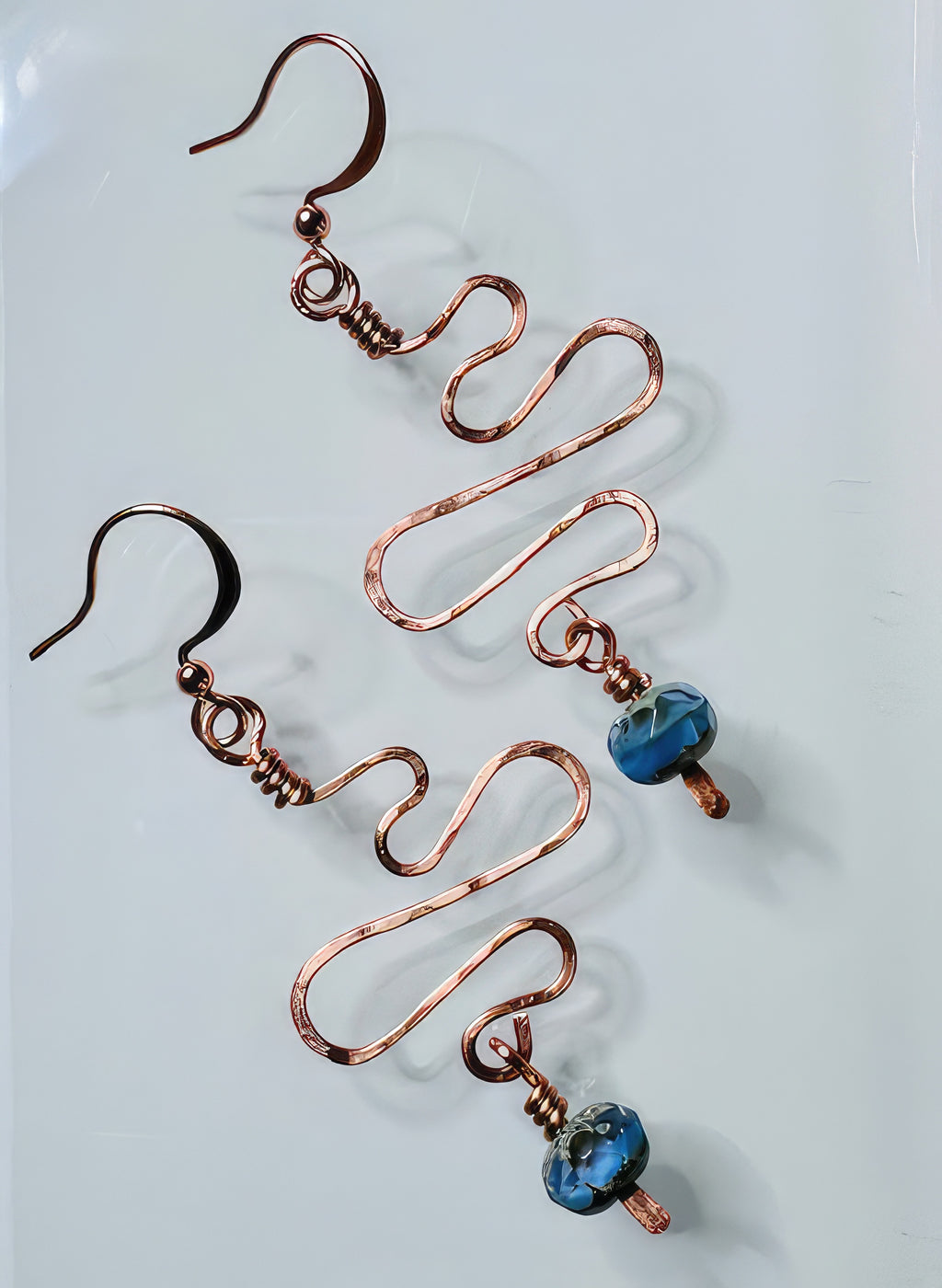 A pair of handcrafted copper earrings with hammered texture and blue faceted glass beads attached to non-tarnish coating wire and ear wires.