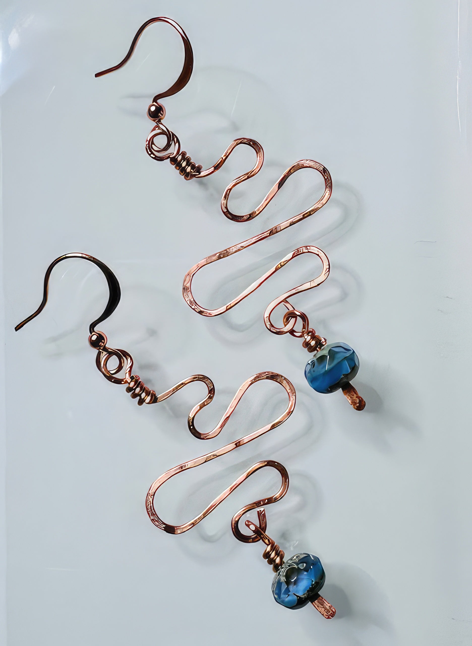 A pair of handcrafted copper earrings with hammered texture and blue faceted glass beads attached to non-tarnish coating wire and ear wires.