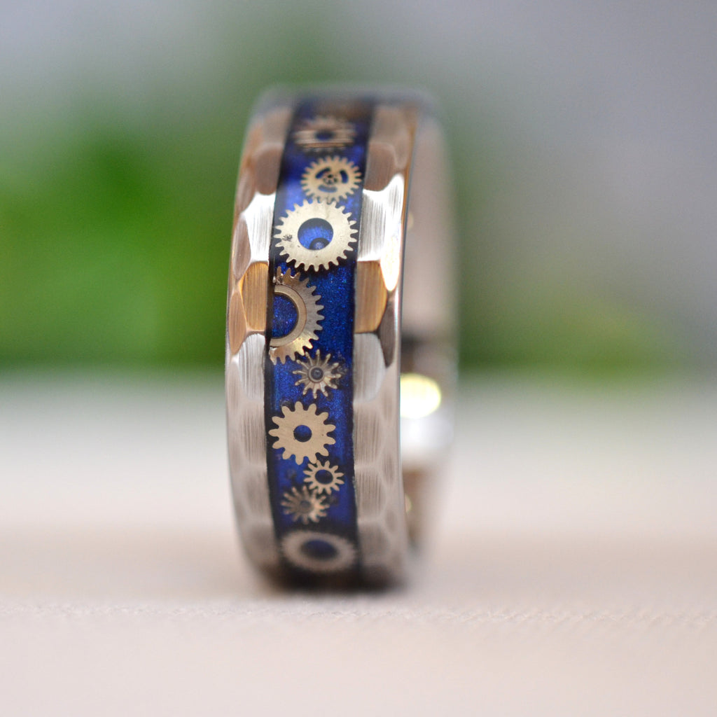 Side profile of the Timekeeper faceted tungsten ring featuring intricate vintage watch gears set into a deep sapphire-blue inlay.