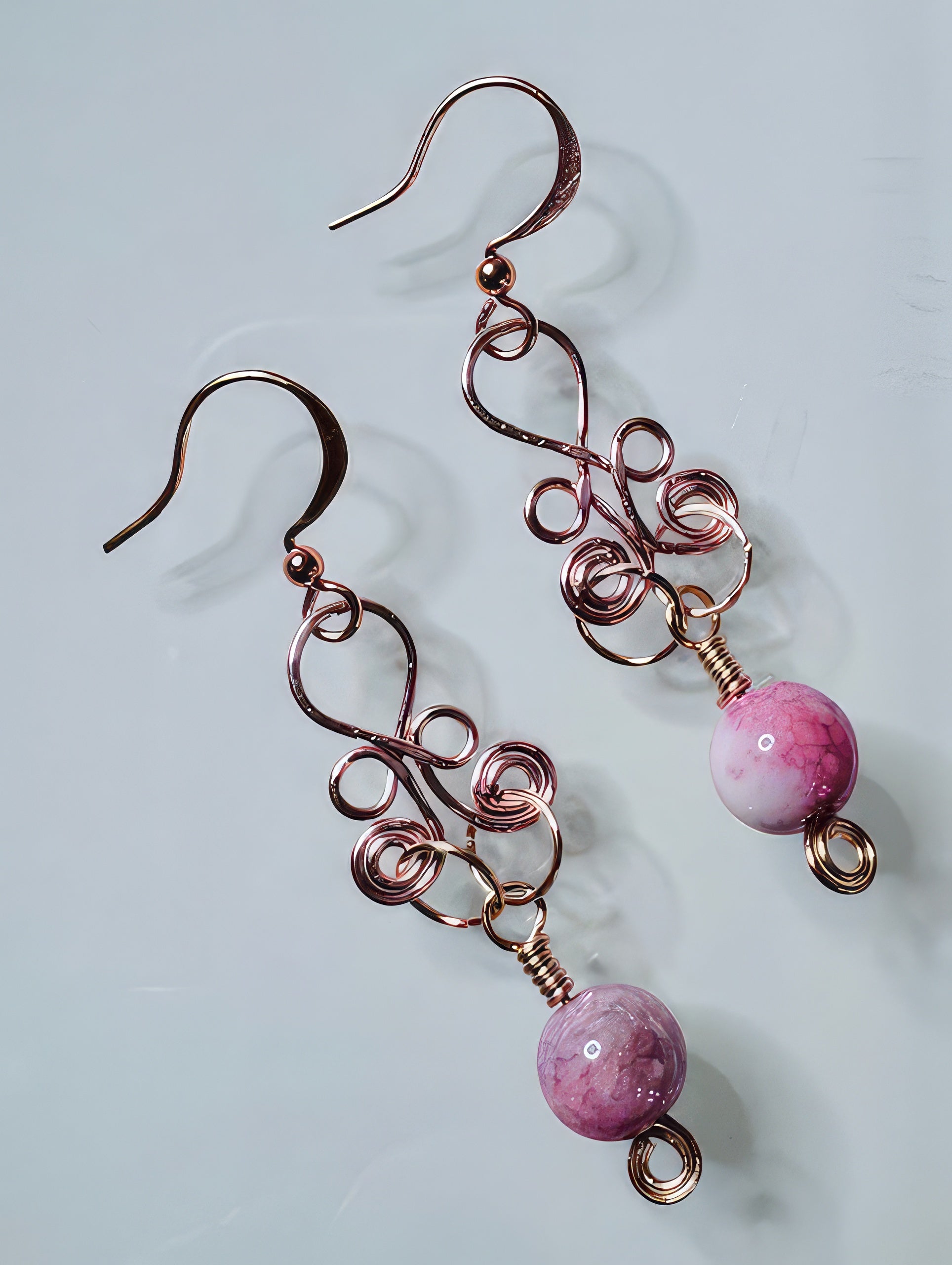 A pair of rose gold-colored earrings with swirly designs and pink rose quartz stones at the bottom.