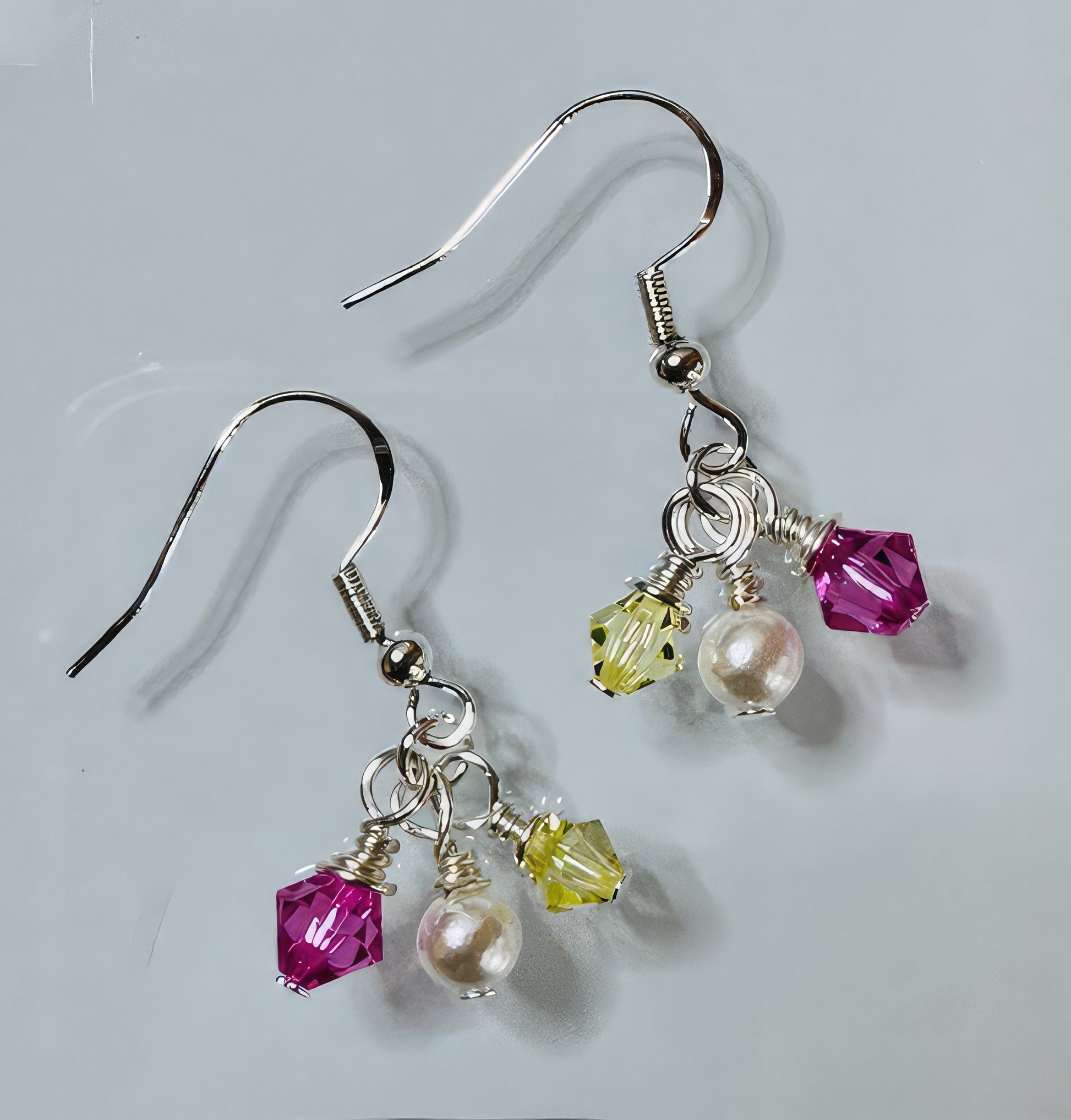 A pair of earrings featuring Swarovski crystals in pink and yellow, along with faux pearls, all connected by silver-coated copper wire on sterling silver ear wires.