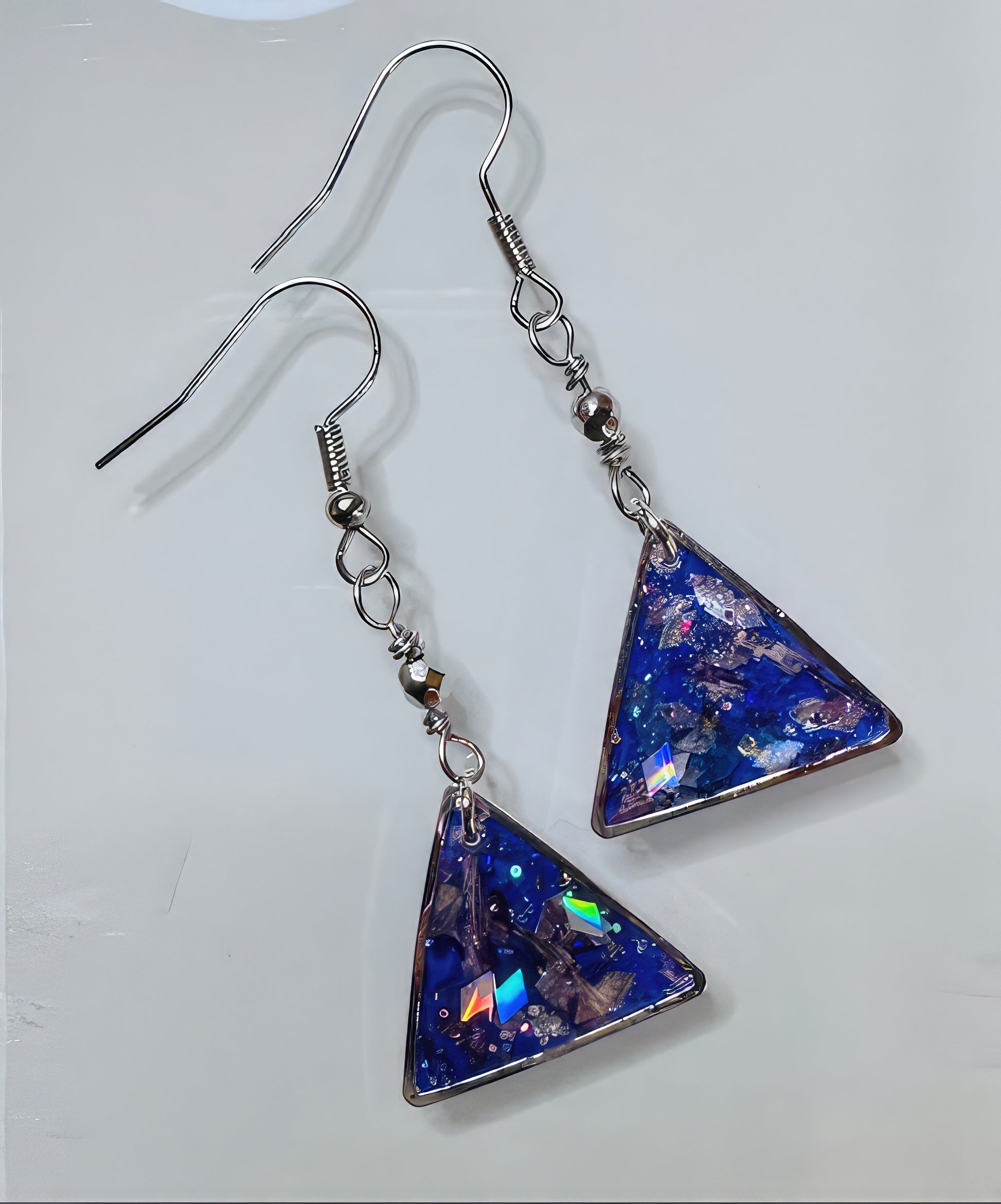 A pair of earrings with a silver-toned triangle design, featuring a lavender background with holographic flakes captured in resin.
