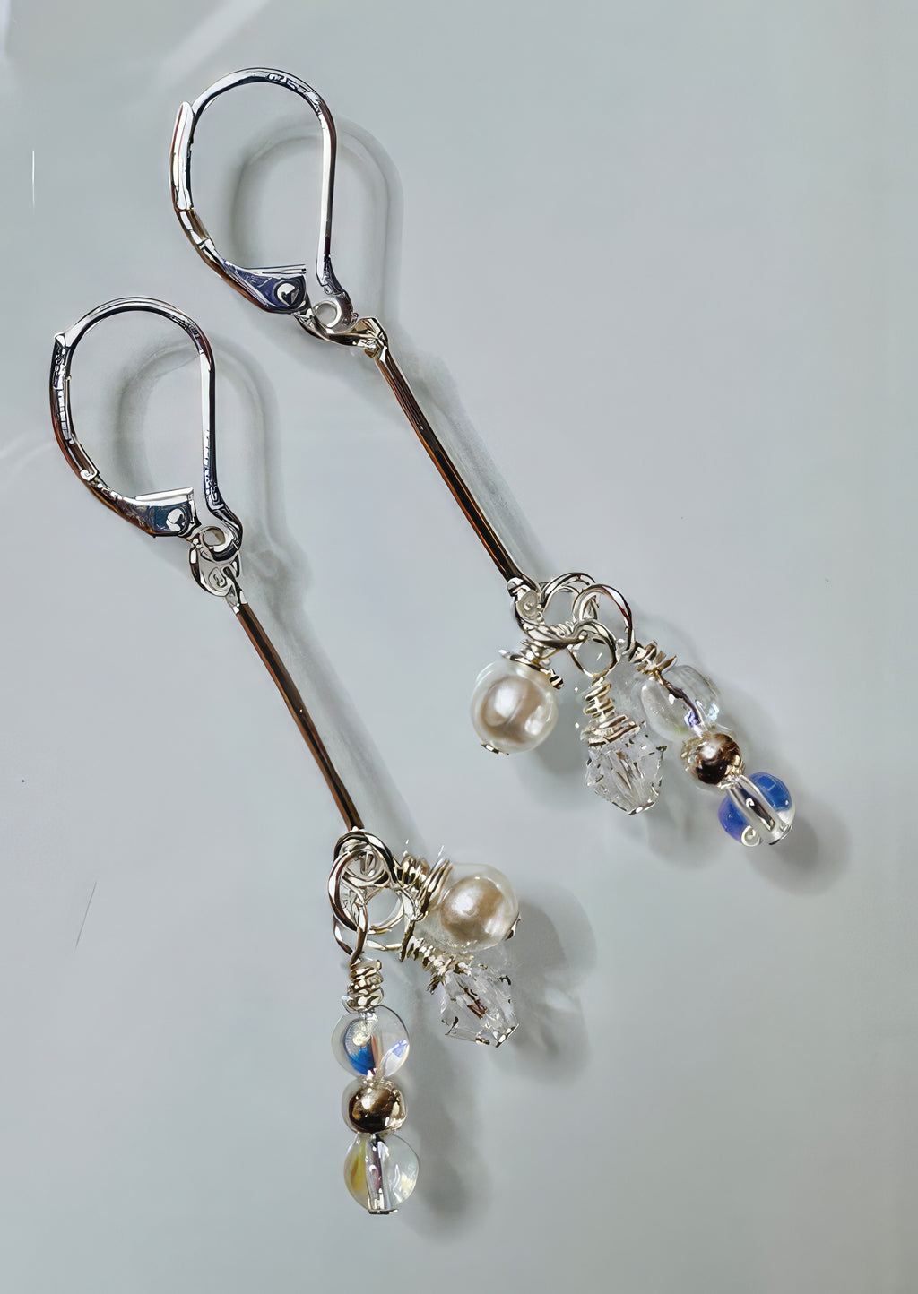 A pair of earrings featuring clear Swarovski crystals, silver-colored beads, and faux cream pearls arranged in a linear drop design with hypoallergenic silver-filled bar and leverback ear wires.