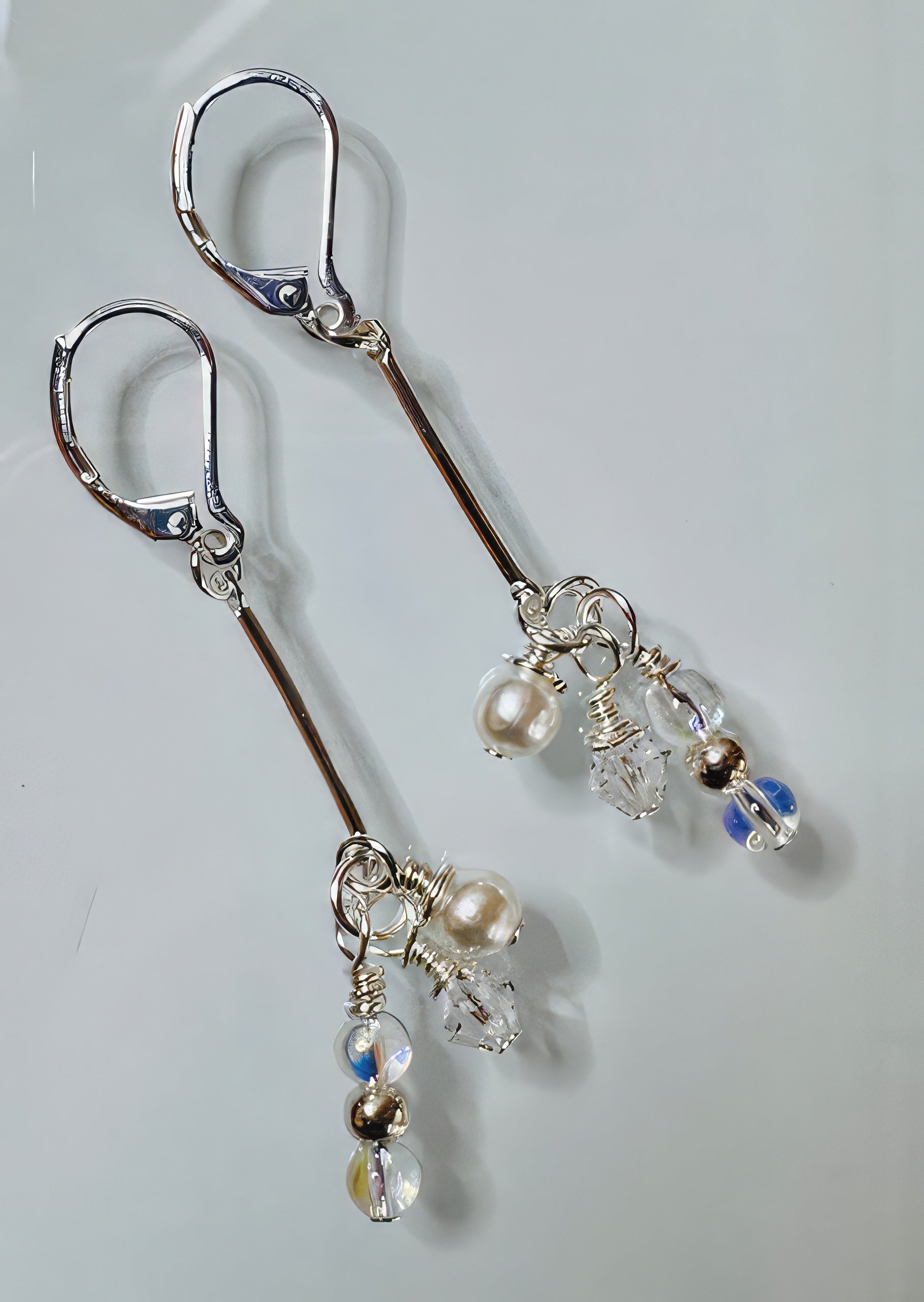 A pair of earrings featuring clear Swarovski crystals, silver-colored beads, and faux cream pearls arranged in a linear drop design with hypoallergenic silver-filled bar and leverback ear wires.