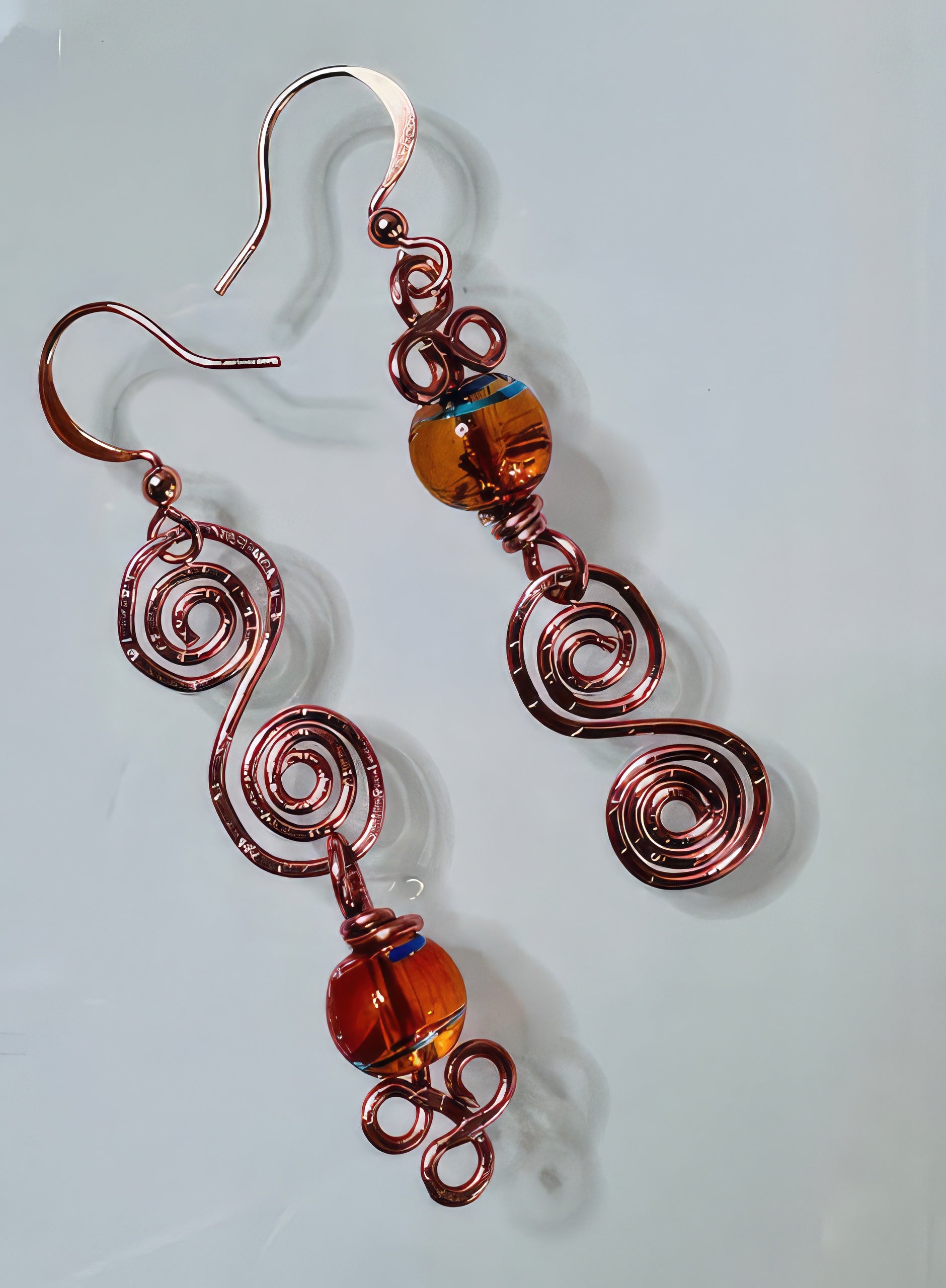 A pair of earrings with spiraled and hammered copper wires and clear amber glass beads.