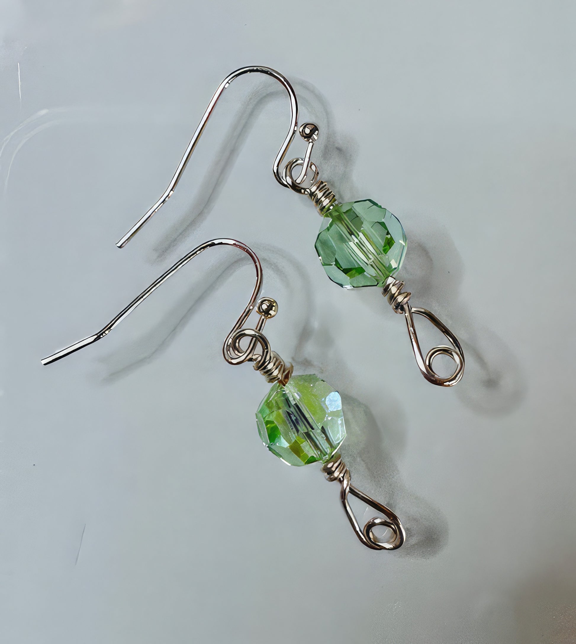 A pair of earrings featuring pale green faceted Czech glass beads on hand-formed wire, with non-tarnish coating and sterling silver ear wires.