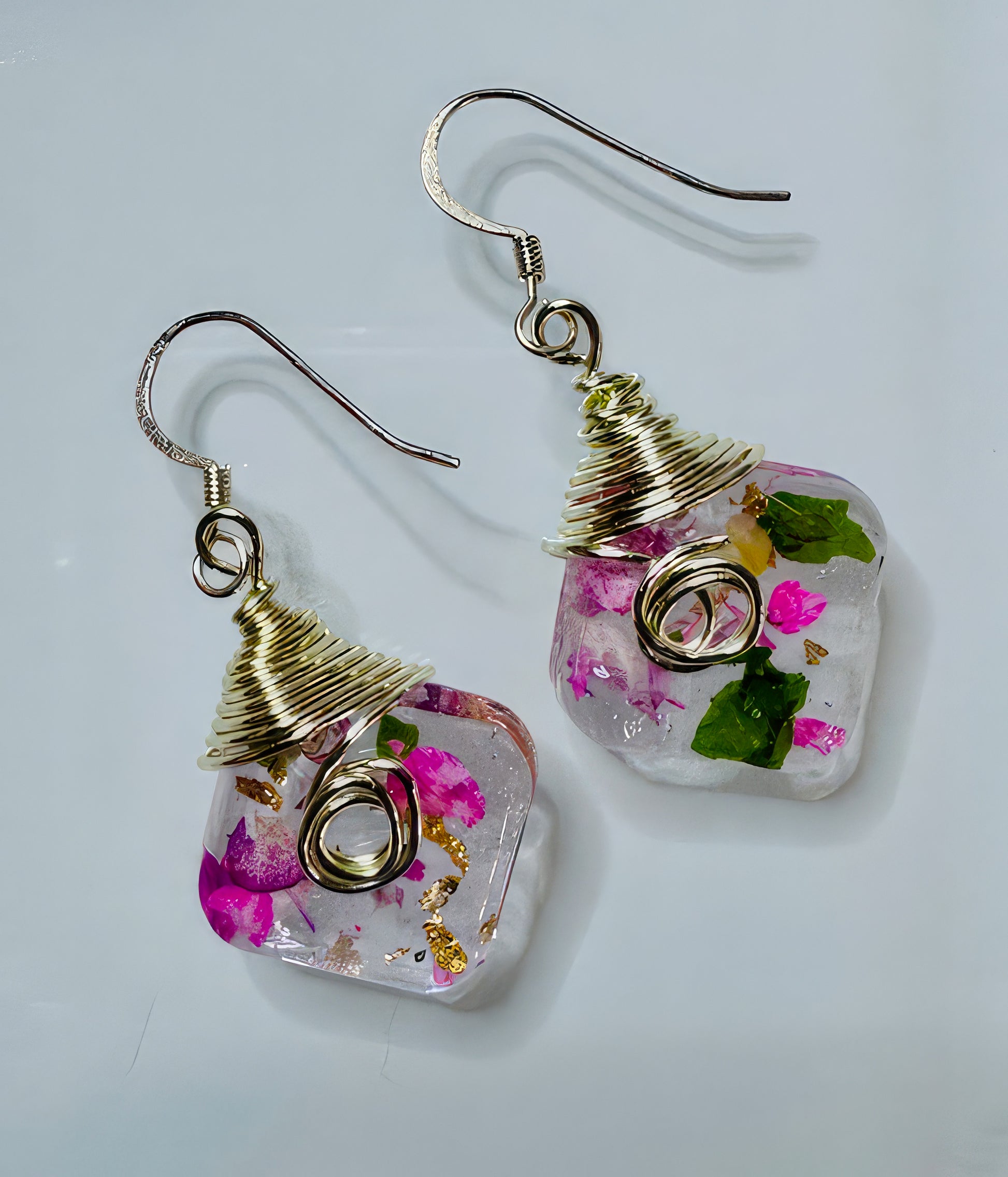 A pair of earrings with clear resin beads, containing encased flower petals and gold leaf, wrapped in gold-filled wire on a white background.