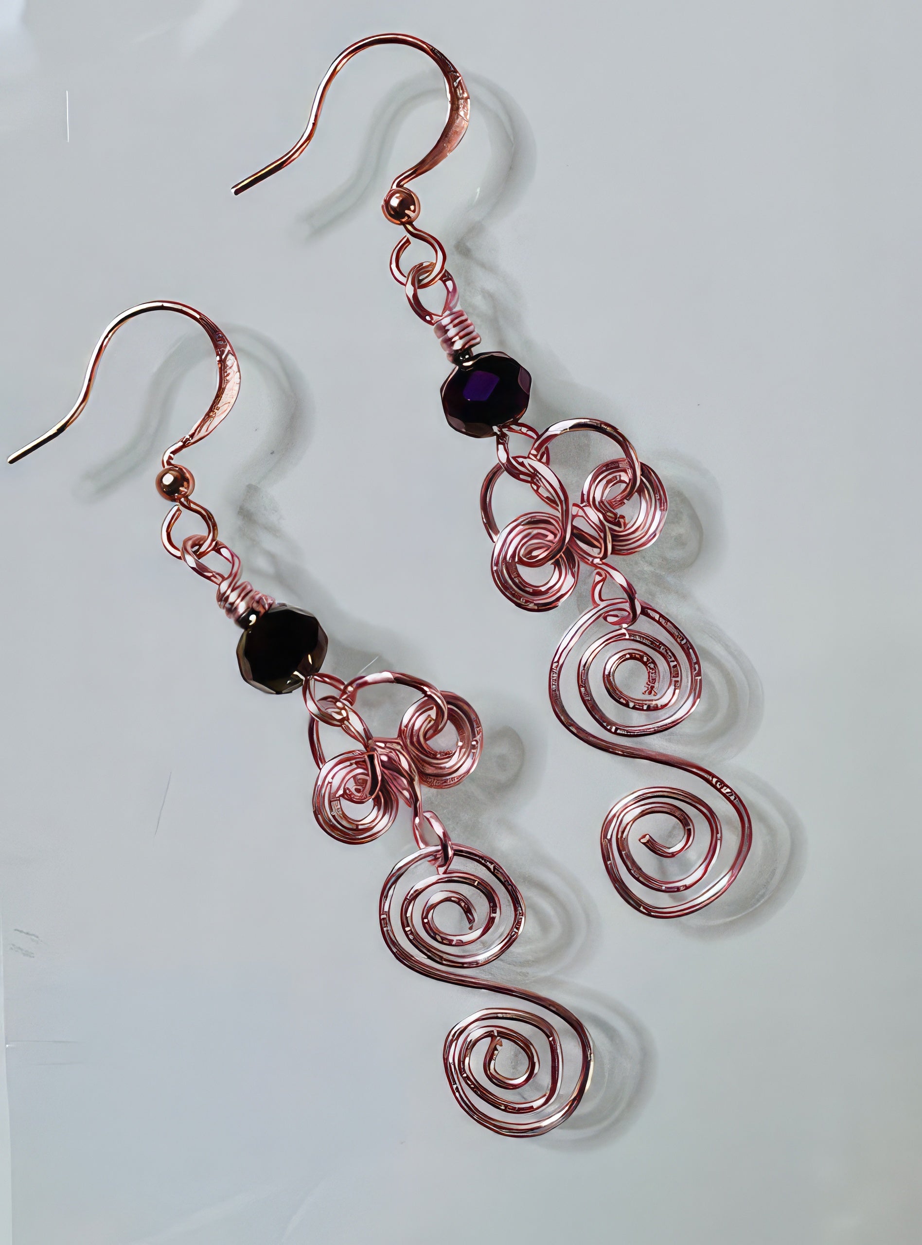 A pair of rose gold copper wire earrings topped with a faceted Czech glass bead, displayed against a white background.