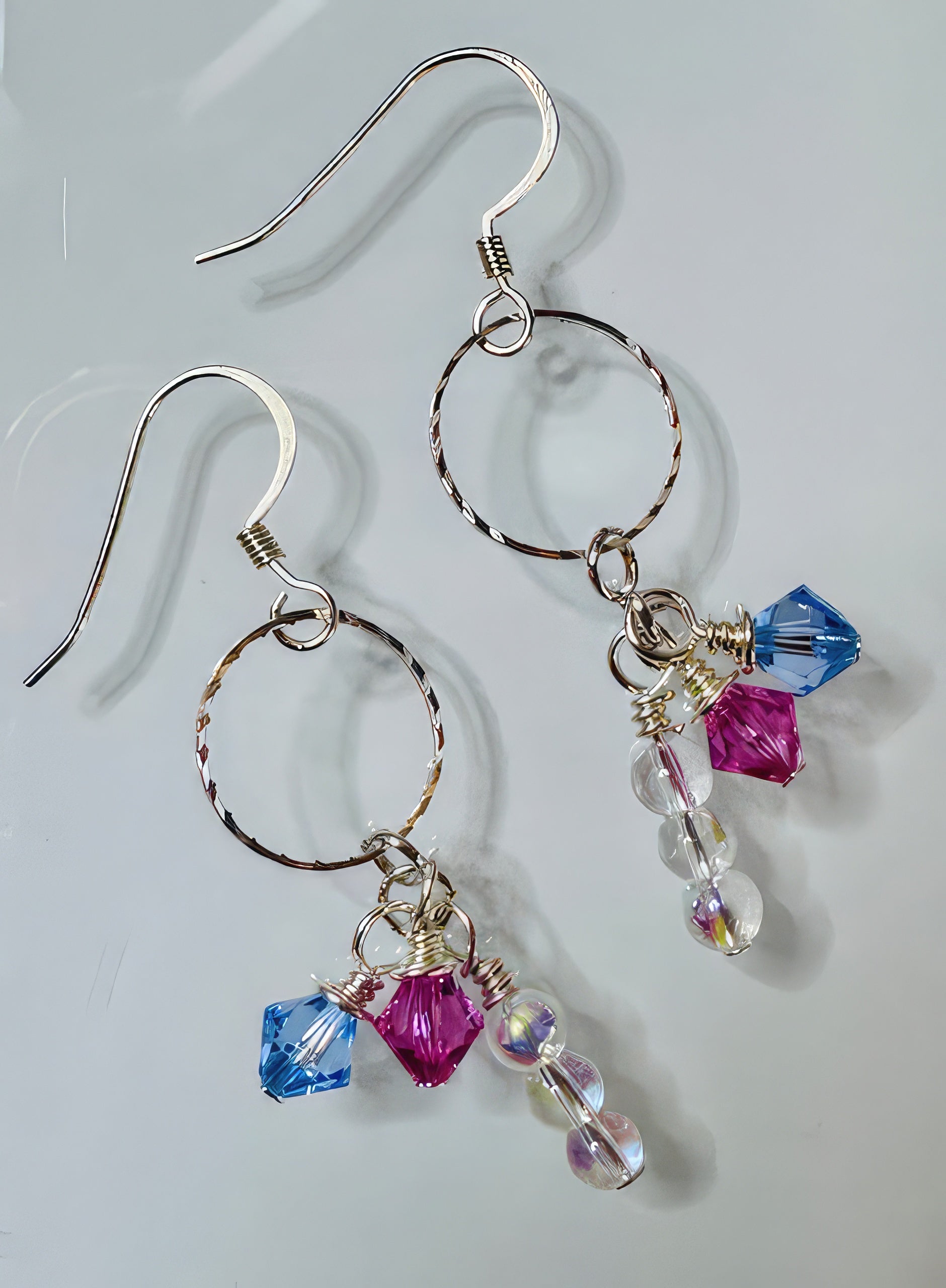 A pair of earrings featuring silver-tone hoops and Swarovski crystals in blue and pink colors, with sterling silver earwire.