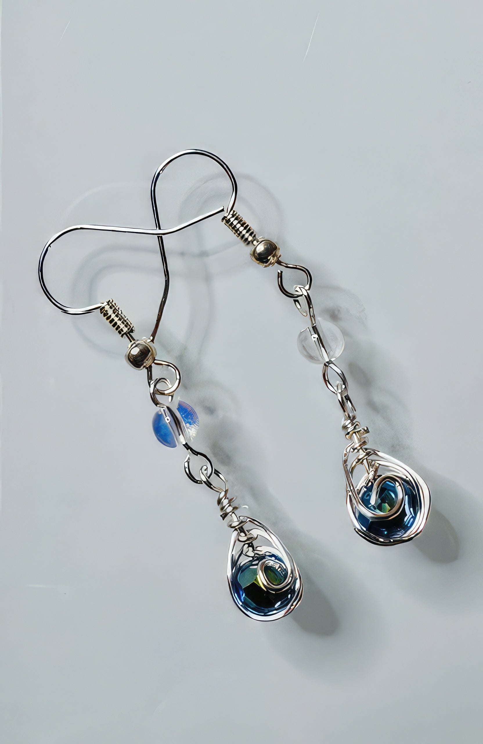 A pair of earrings featuring medium blue Czech glass beads with clear accents, wrapped in silver-coated copper wire, suspended from sterling silver ear wires.