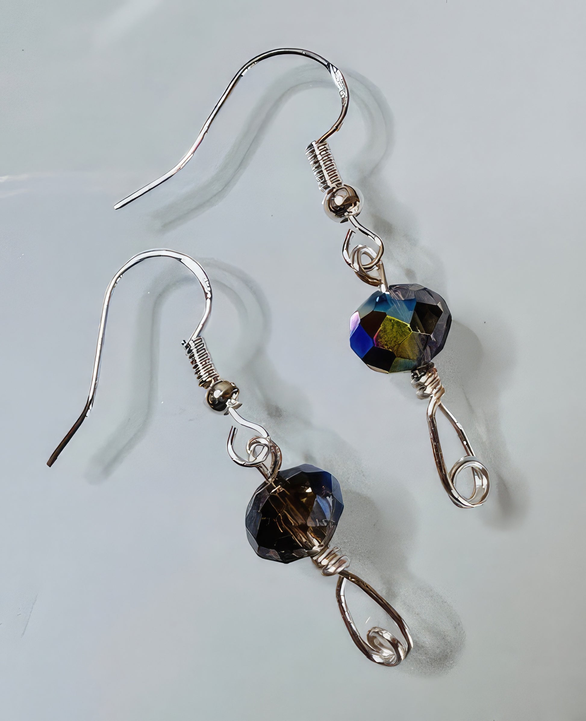 A pair of earrings featuring a faceted Czech glass bead in shades of purple, green and clear, attached to hand formed wire with sterling silver earwire.