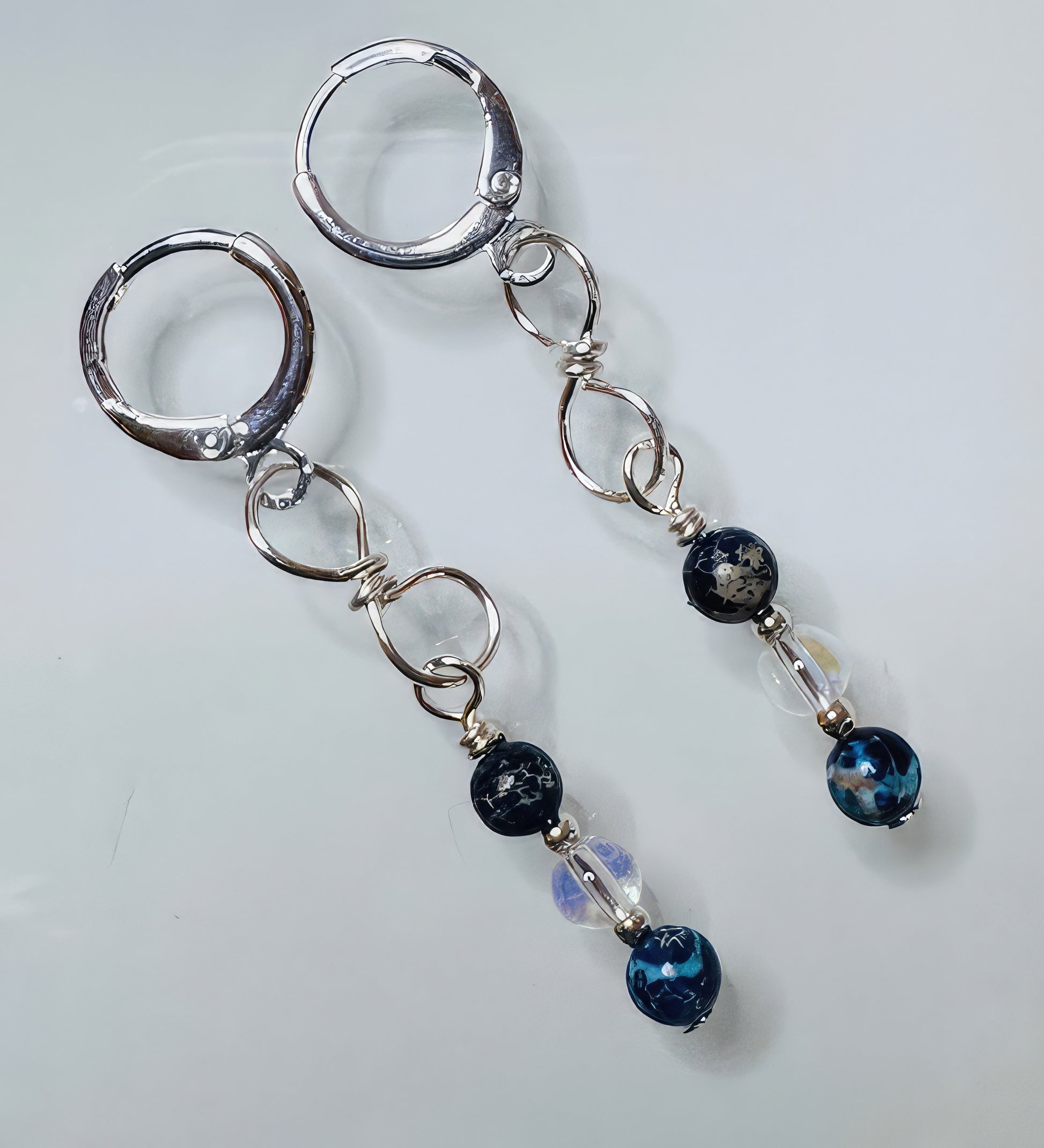 A pair of earrings featuring twisted wire craftsmanship with clear glass beads and dark blue natural stones, attached to hypoallergenic nickel-free leverback ear wires.