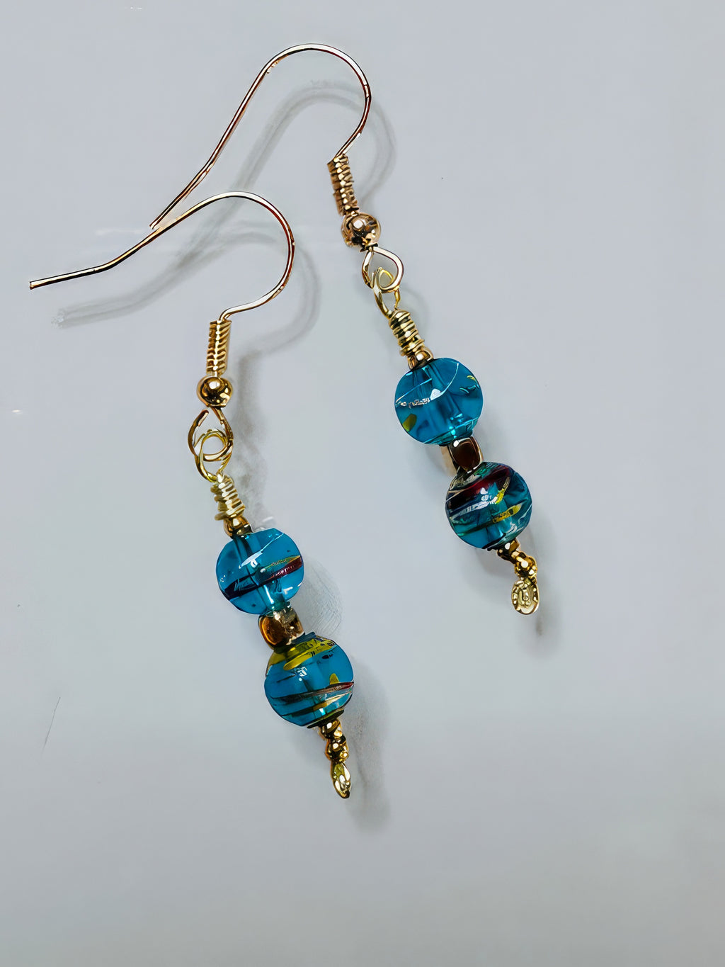 A pair of earrings featuring gold-colored wire and beads with a teal color, along with a hint of red, arranged in an elegant drop design.