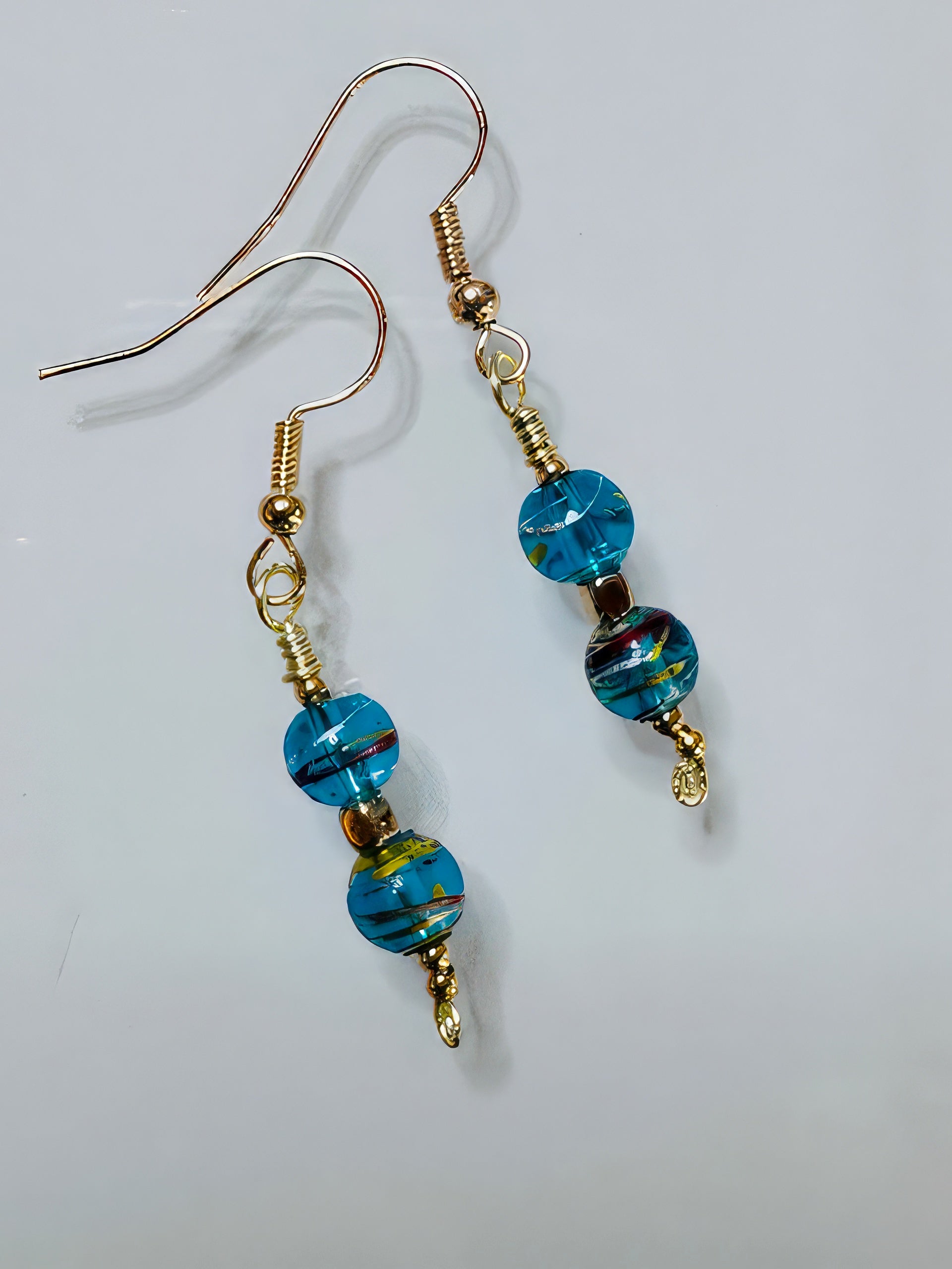 A pair of earrings featuring gold-colored wire and beads with a teal color, along with a hint of red, arranged in an elegant drop design.