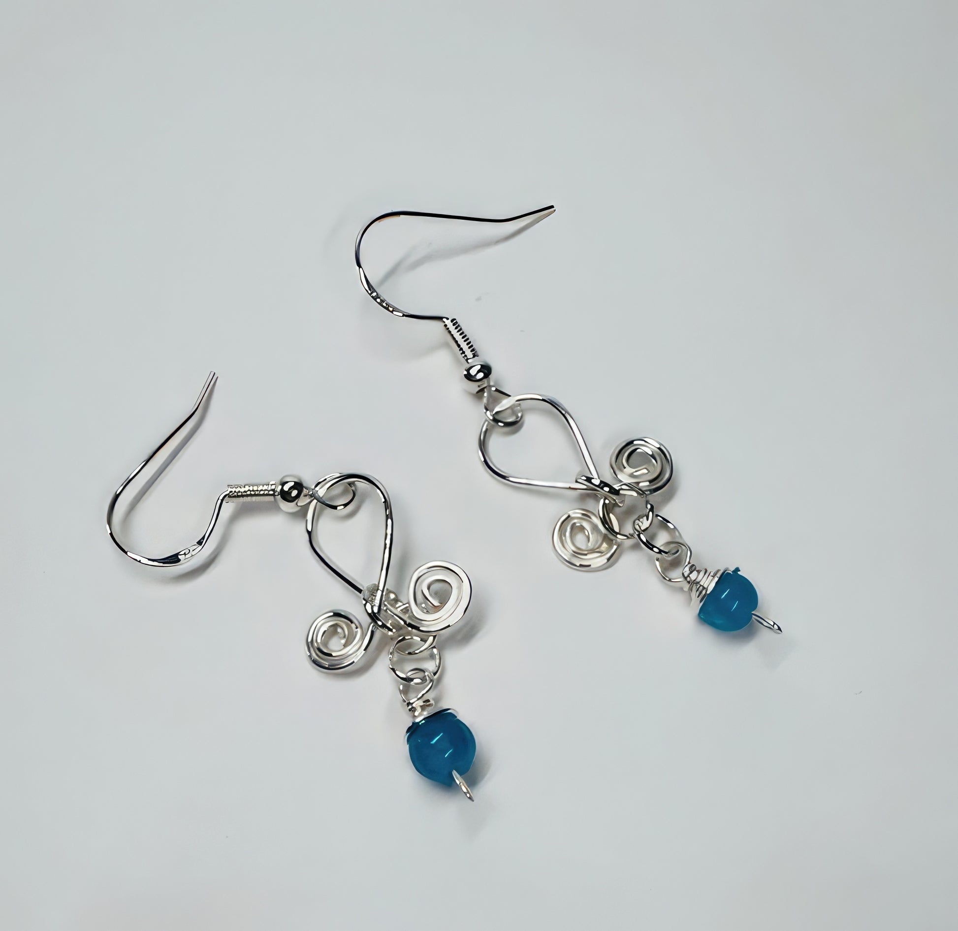 A pair of earrings featuring wrapped blue stone with silver-colored wire and sterling silver French ear wires