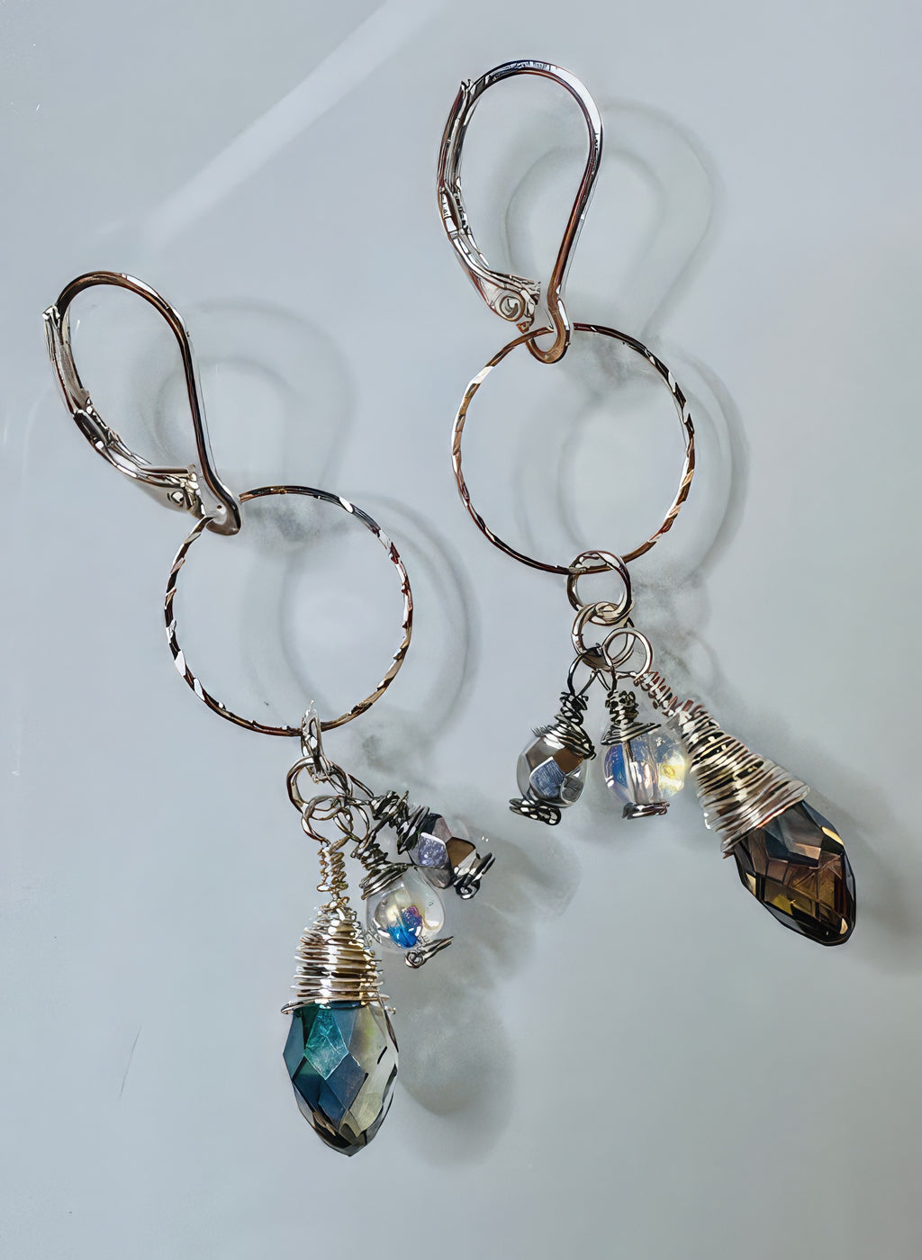 A pair of earrings featuring silver-filled faceted hoops and clear round beads with iridescent teardrop-shaped glass beads attached to hypoallergenic leverback ear wires.