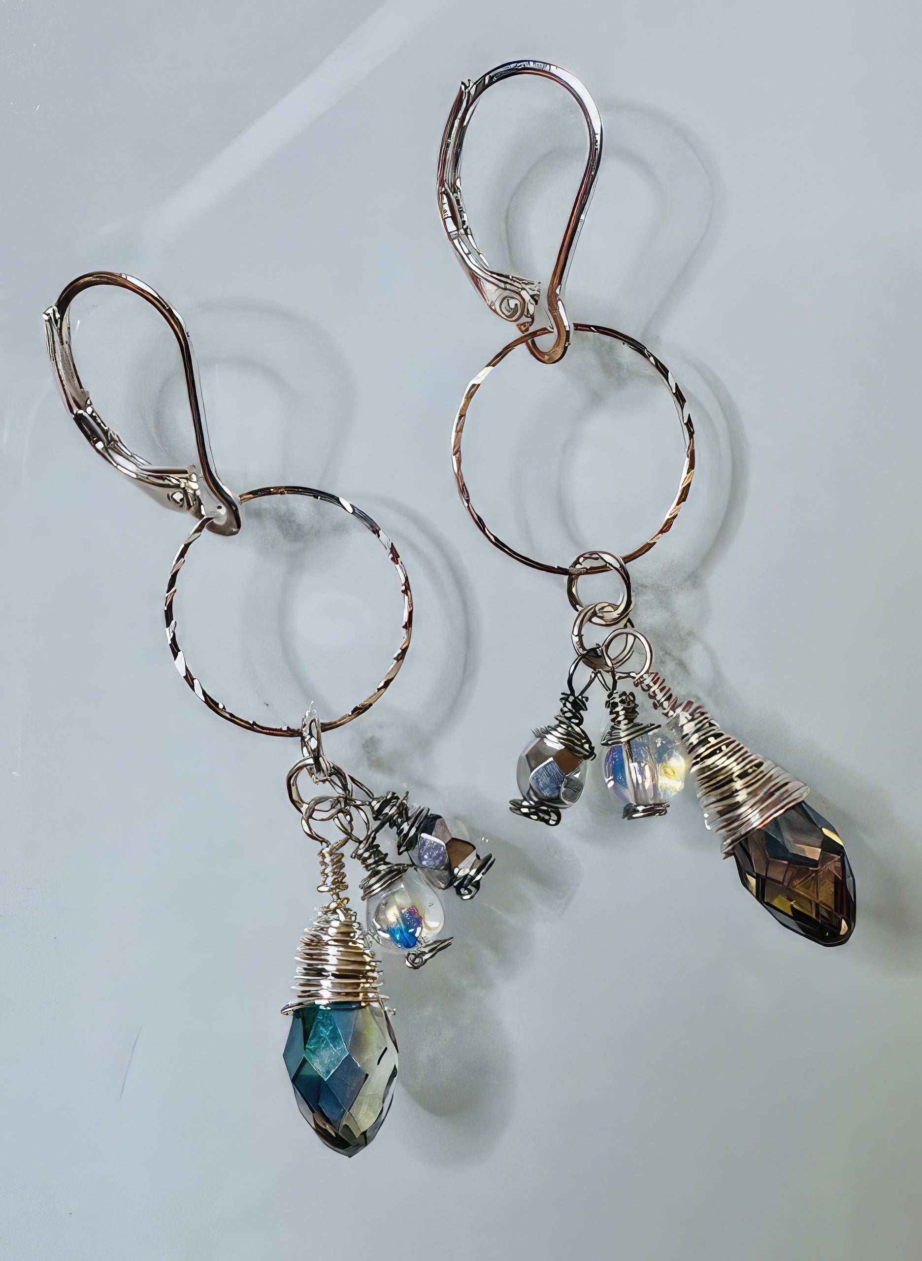 A pair of earrings featuring silver-filled faceted hoops and clear round beads with iridescent teardrop-shaped glass beads attached to hypoallergenic leverback ear wires.