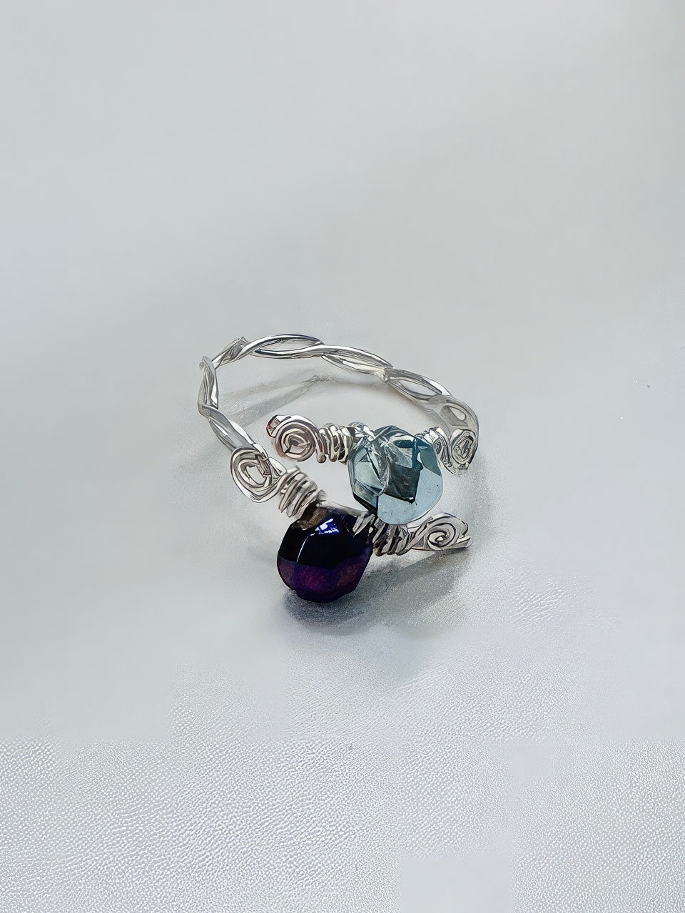 Hand twisted silver wire formed into an alluring ring with baby blue and deep purple faceted beads